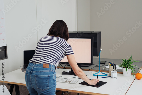 Businesswoman standing leaning over a desk working on a computer © contrastwerkstatt