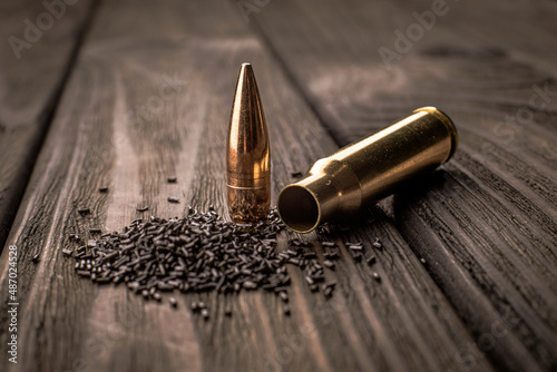 Macro shot of a cartridge, cartridge case and gunpowder on a wooden background, soft focus.