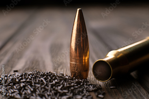 Macro shot of a cartridge, cartridge case and gunpowder on a wooden background with limited depth of field, soft focus