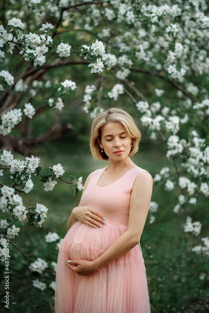 a pregnant young woman in a spring blooming garden next to a blooming apple tree. Her eyes are closed. a pregnant young woman in a spring blooming garden next to a blooming apple tree. Her eyes are closed.