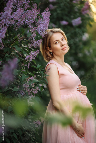 a young pregnant woman next to a lilac bush
