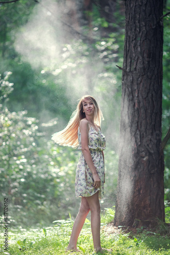 Blonde girl in a light airy dress, barefoot at dawn in a summer forest