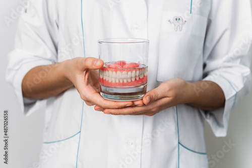 Prosthesis in a glass with a solution. Dental prosthesis care. Full removable plastic denture of the jaws. Two acrylic dentures. Upper and lower jaws with fake teeth. Dentures or false teeth, close-up photo