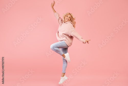 Playful caucasian woman jumping and having fun over pink studio background, lady posing in mid-air