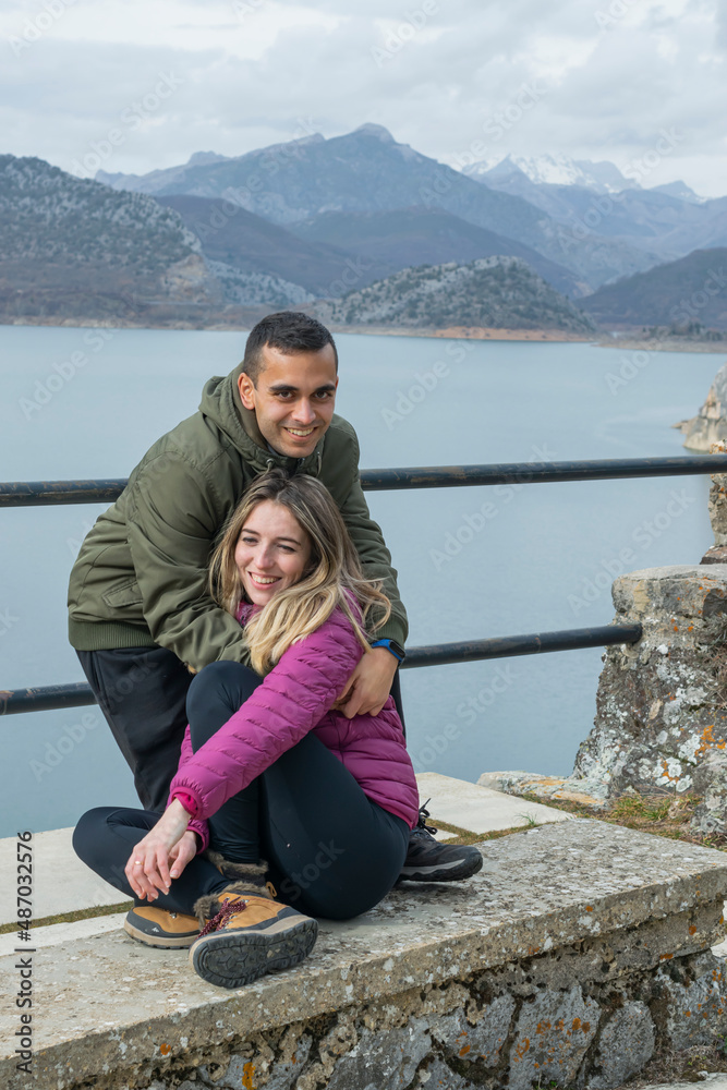 Pareja joven enamorada sentada y abrazada en un banco con las montañas nevadas de fondo Pareja joven enamorada sentada y abrazada en un banco con las montañas nevadas de fondo