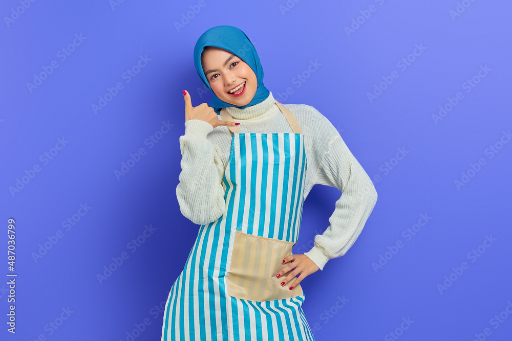 Portrait of cheerful young housewife woman in hijab and striped apron doing phone gesture like says call me back isolated on purple background. People housewife muslim lifestyle concept Portrait of cheerful young housewife woman in hijab and striped apron doing phone gesture like says call me back isolated on purple background. People housewife muslim lifestyle concept