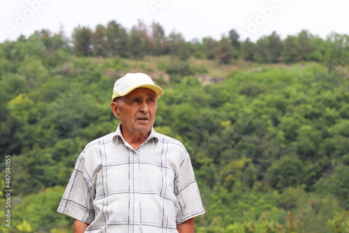 Portrait of elderly man on green mountain background. Life in village, travel in old age