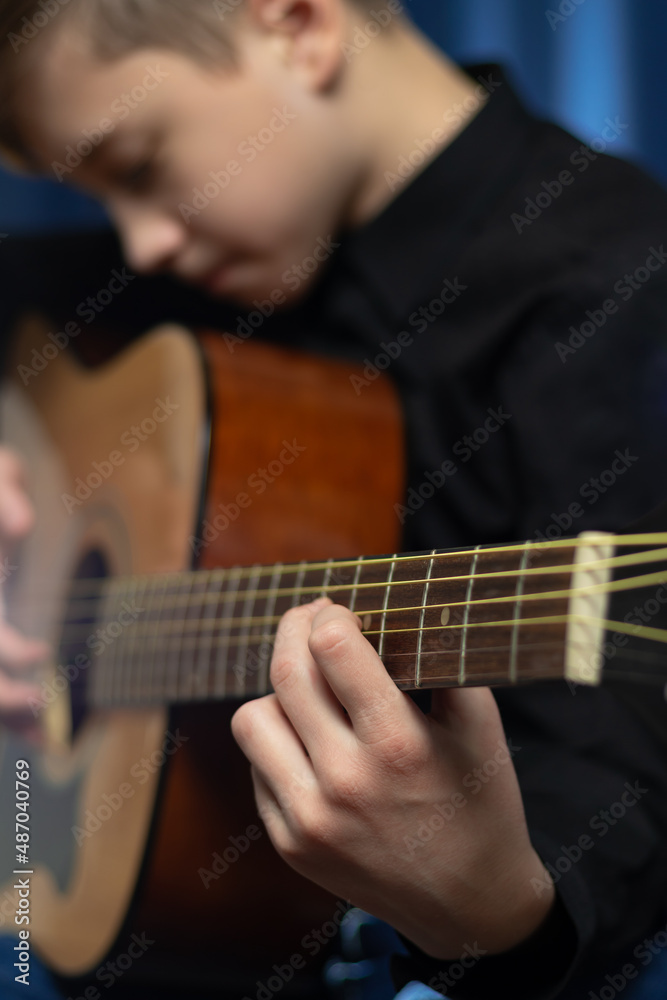 A teenager guy in a black shirt plays the acoustic guitar at a concert on a blue background. Hobby. Musical instruments. Selective focus. Portrait