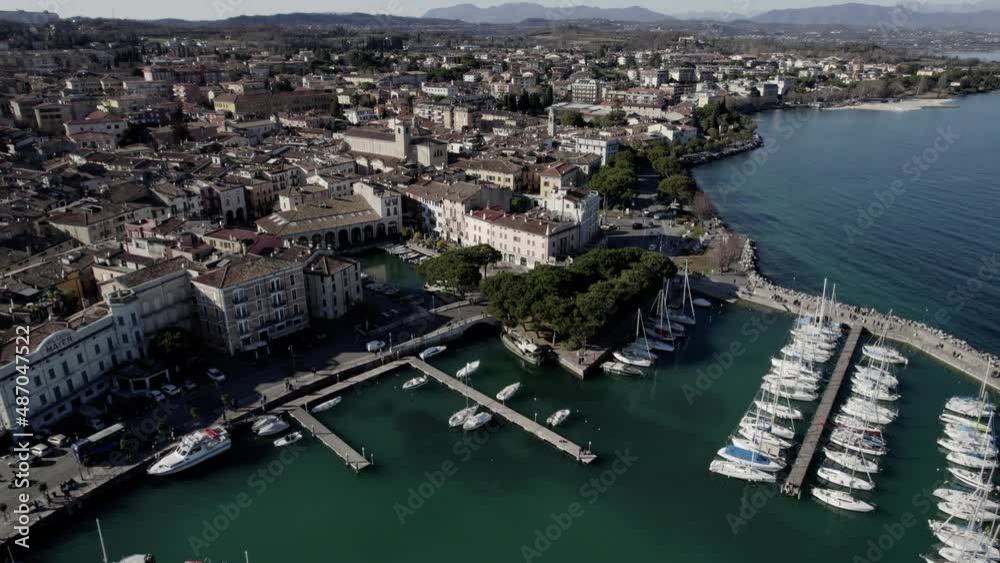 Aerial image filmed with a drone showing the town of Desenzano del Garda located on the shores of Lake Garda, northern Italy. Small port with sailing boats. Boats and yachts on the lake. Aerial image filmed with a drone showing the town of Desenzano del Garda located on the shores of Lake Garda, northern Italy. Small port with sailing boats. Boats and yachts on the lake.