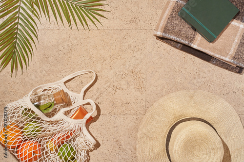 Fototapeta Naklejka Na Ścianę i Meble -  Summer sunny beach concept flat lay.Hat, string bag with fruits and lemonade, palm leaves and accessories. High quality photo
