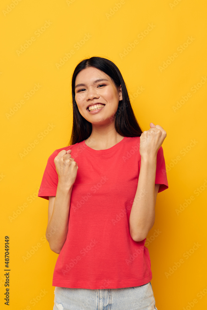woman with Asian appearance in a red t-shirt posing emotions fun yellow background unaltered woman with Asian appearance in a red t-shirt posing emotions fun yellow background unaltered