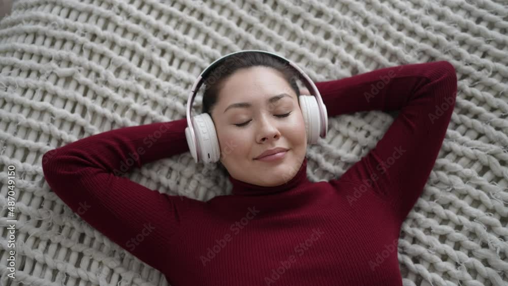 Young calm ethnic woman chilling on comfortable sofa with closed eyes wearing wireless headphones, asian girl enjoys listening chill music and audio sound relaxing and meditating at bedroom. Young calm ethnic woman chilling on comfortable sofa with closed eyes wearing wireless headphones, asian girl enjoys listening chill music and audio sound relaxing and meditating at bedroom.