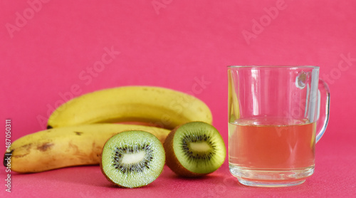 ripe kiwi in a banana section and a cup with juice on a pink background
