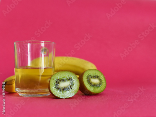 ripe kiwi in a banana section and a cup with juice on a pink background