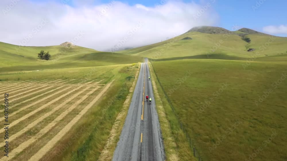 People Biking On Asphalt Road With Green Field Landscape Scenery In San Luis Obispo, California. wide aerial People Biking On Asphalt Road With Green Field Landscape Scenery In San Luis Obispo, California. wide aerial