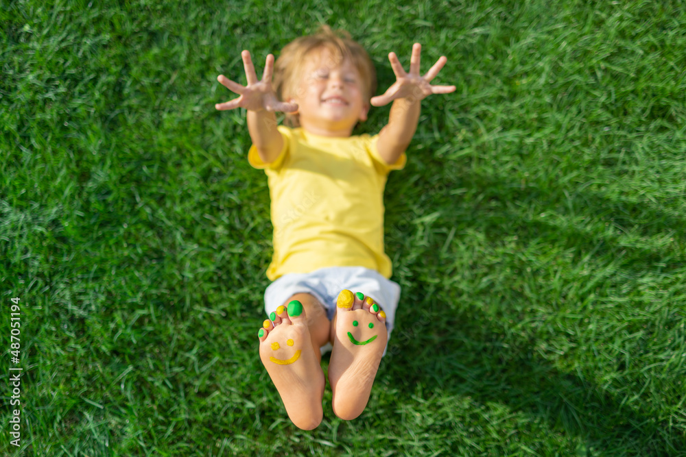 Happy child with smile on feet lying on green spring grass Happy child with smile on feet lying on green spring grass