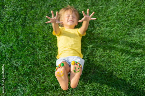 Happy child with smile on feet lying on green spring grass
