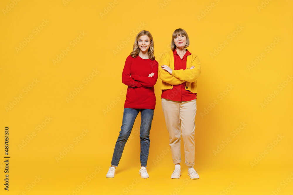 Full body smiling happy cool woman 50s in red shirt have fun with teenager girl 12-13 years old. Grandmother granddaughter hold hands crosed folded isolated on plain yellow background. Family concept Full body smiling happy cool woman 50s in red shirt have fun with teenager girl 12-13 years old. Grandmother granddaughter hold hands crosed folded isolated on plain yellow background. Family concept