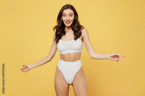 Surprised amazed impressed happy lovely attractive young brunette woman 20s in white underwear with perfect fit body standing posing look camera isolated on plain yellow background studio portrait © ViDi Studio