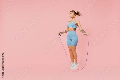 Full size young sporty athletic fitness trainer instructor woman wear blue tracksuit spend time in home gym using skipping rope isolated on pastel plain light pink background. Workout sport concept.