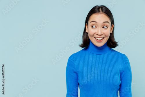 Blithesome joyful smiling young woman of Asian ethnicity 20s years old wears blue shirt looking aside isolated on plain pastel light blue background studio portrait. People emotions lifestyle concept.