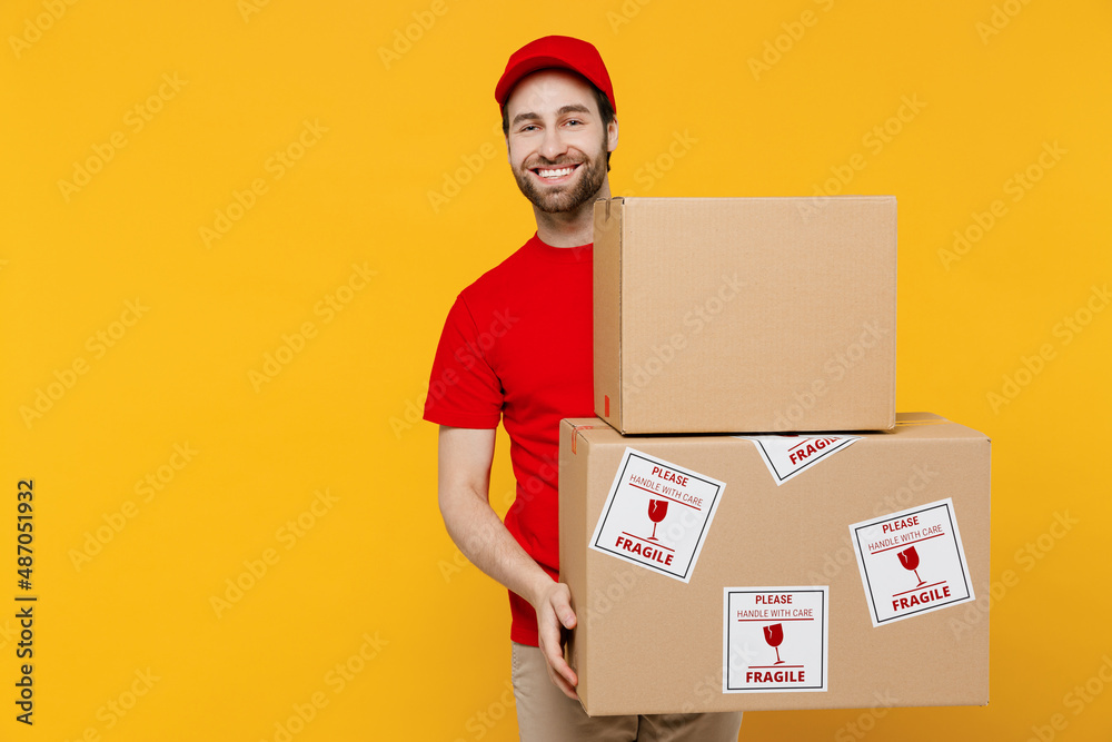 Professional happy delivery guy employee man in red cap T-shirt uniform workwear work as dealer courier hold cardboard box with fragile text isolated on plain yellow background studio Service concept Professional happy delivery guy employee man in red cap T-shirt uniform workwear work as dealer courier hold cardboard box with fragile text isolated on plain yellow background studio Service concept