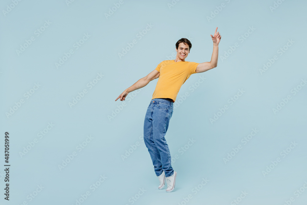 Full body smiling happy cool young man 20s wear yellow t-shirt leaning back stand on toes dance fooling around isolated on plain pastel light blue background studio portrait. People lifestyle concept.