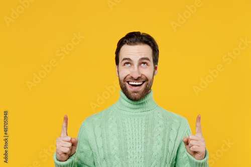 Young smiling happy fun cool man 20s in mint knitted sweater point index finger overhead on workspace area mock up isolated on plain yellow background studio portrait People lifestyle fashion concept