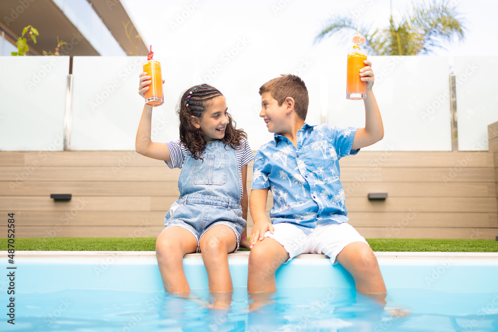 Two funny kids making a toast with orange juice in the swimming pool