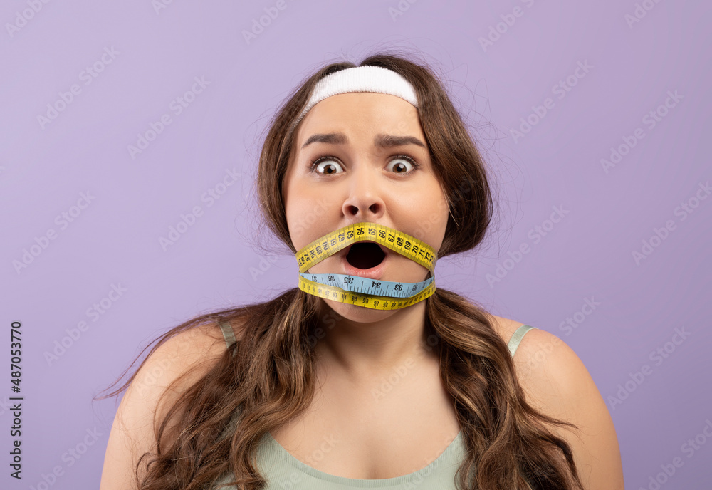 Shocked scared young european plus size lady in sportswear with open mouth wrapped in measuring tape Shocked scared young european plus size lady in sportswear with open mouth wrapped in measuring tape