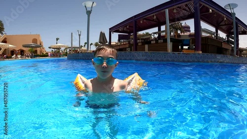 A boy-child swims, dives in the pool under water, looks at the camera