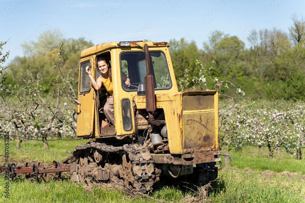 Old Tractor in the Field. Farmer in Old-fashioned tractor sowing crops at field. Woman driving small tractor in field and waving hand Old Tractor in the Field. Farmer in Old-fashioned tractor sowing crops at field. Woman driving small tractor in field and waving hand