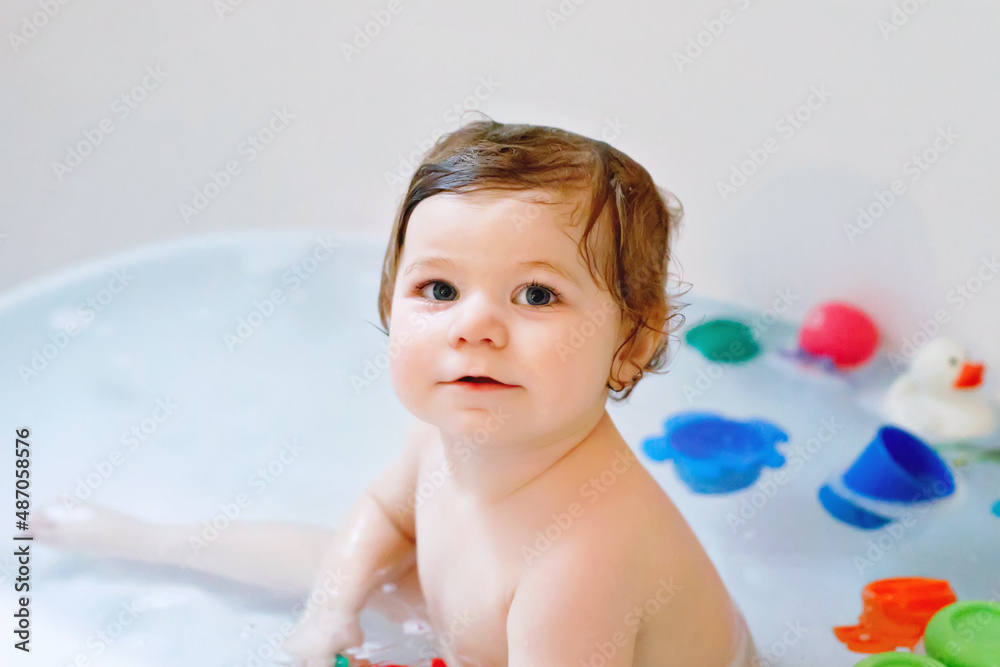 Cute adorable baby girl taking foamy bath in bathtub. Toddler playing with bath rubber toys. Cute adorable baby girl taking foamy bath in bathtub. Toddler playing with bath rubber toys.