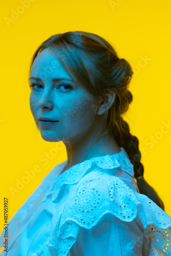 Close-up portrait of young pretty girl with freckles posing isolated on yellow background in neon. Concept of emotions, facial expressions