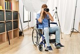 Young redhead man photographer sitting on wheelchair using professional camera at clinic
