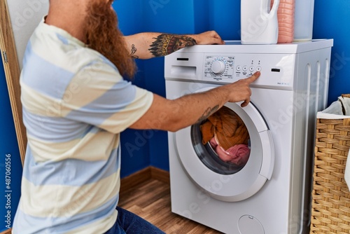 Murais de parede Young redhead man turning on washing machine at laundry room