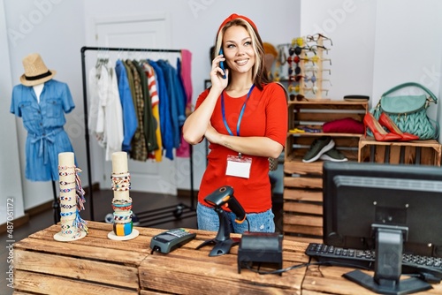 Young caucasian shopkeeper woman smiling happy talking on the smartphone working at clothing store.