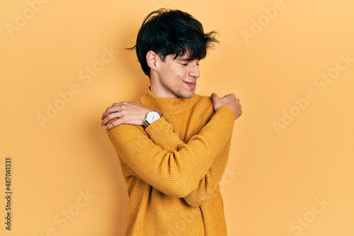 Handsome hipster young man wearing casual yellow sweater hugging oneself happy and positive, smiling confident. self love and self care © Krakenimages.com