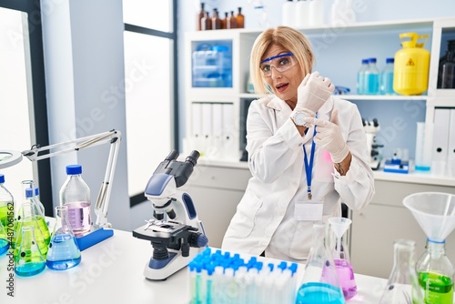 Fototapeta Naklejka Na Ścianę i Meble -  Middle age blonde woman working at scientist laboratory in hurry pointing to watch time, impatience, looking at the camera with relaxed expression