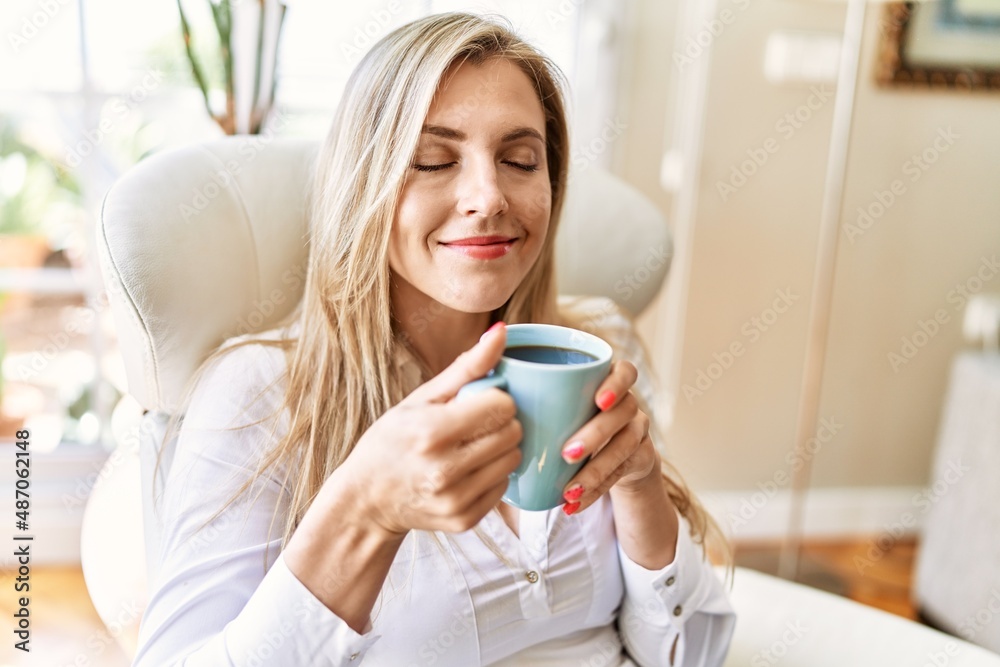 Young blonde woman drinking cup of coffee sitting on armchair at home. Young blonde woman drinking cup of coffee sitting on armchair at home.
