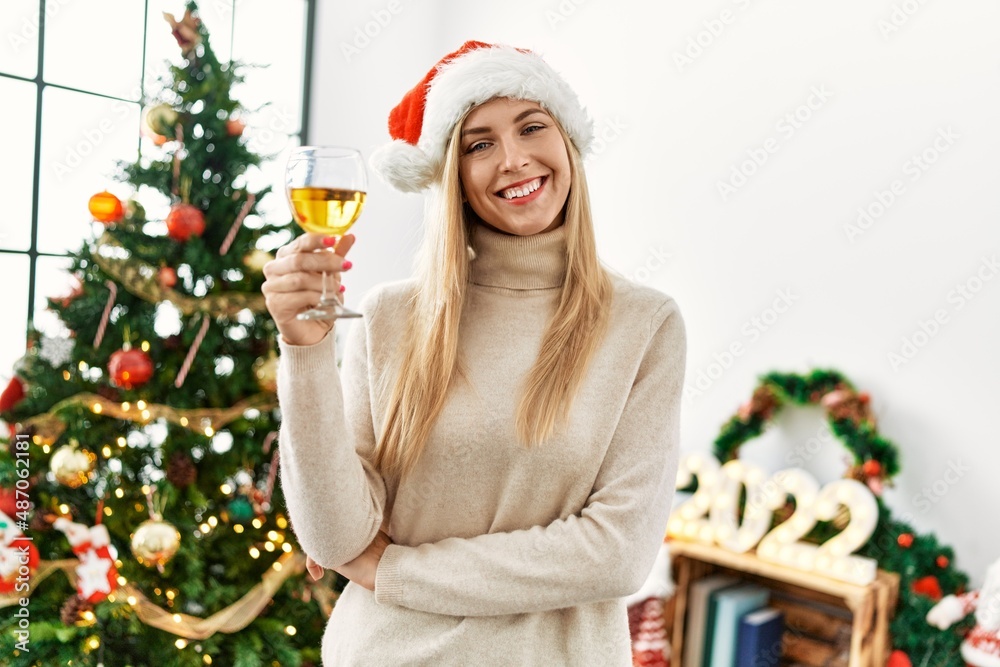 Young blonde woman toasting with champagne standing by christmas tree at home Young blonde woman toasting with champagne standing by christmas tree at home