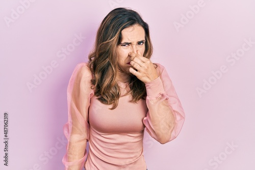Young hispanic girl wearing casual clothes smelling something stinky and disgusting, intolerable smell, holding breath with fingers on nose. bad smell