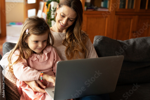 Cheerful little girl using laptop. Beautiful girl watching cartoon with mom.. © JustLife