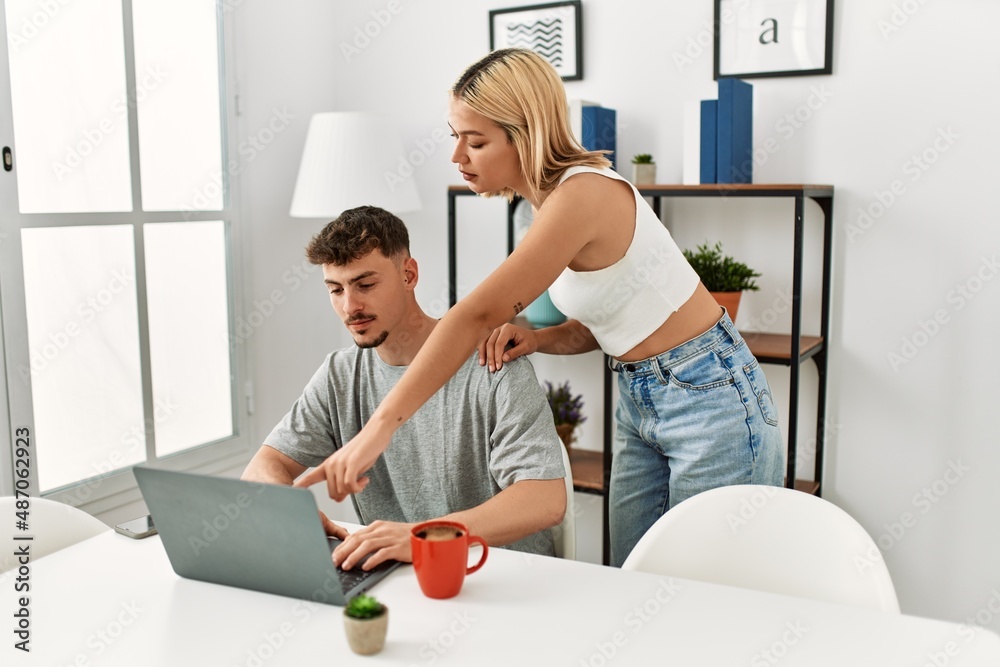 Fototapeta premium Young caucasian couple using laptop and drinking coffee sitting on the table at home.
