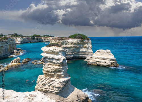 Melendugno,province of Lecce, Puglia, Italy. August 2021. The stacks of Sant'Andrea are a point of naturalistic attraction: the amazing landscape suggests a tropical destination. People taking a bath. photo