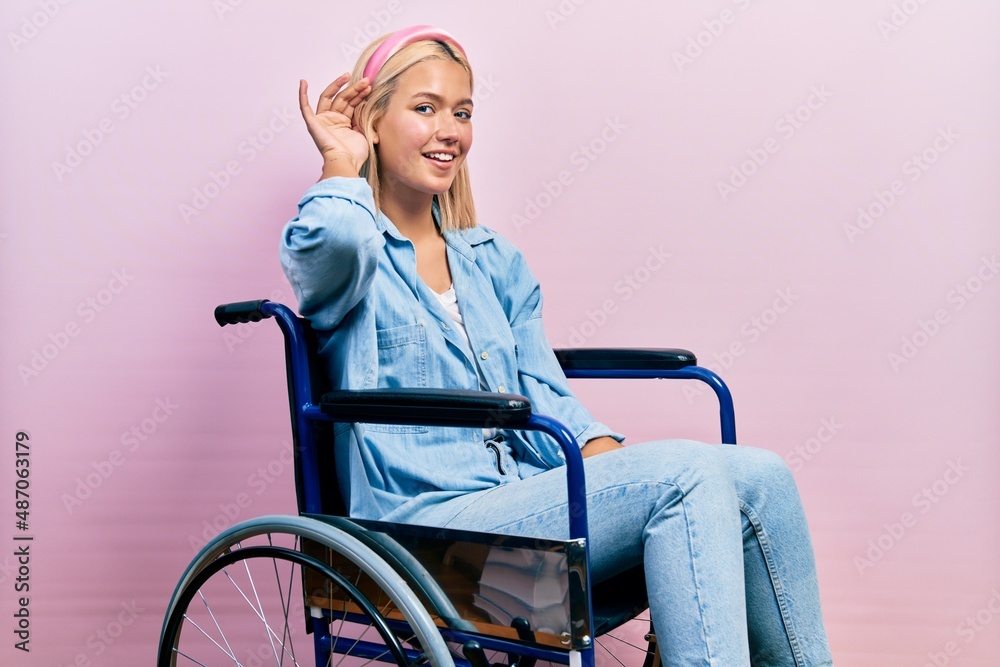 Beautiful blonde woman sitting on wheelchair smiling with hand over ear listening an hearing to rumor or gossip. deafness concept. Beautiful blonde woman sitting on wheelchair smiling with hand over ear listening an hearing to rumor or gossip. deafness concept.