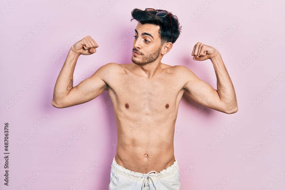 Fototapeta premium Young hispanic man wearing swimwear shirtless showing arms muscles smiling proud. fitness concept.