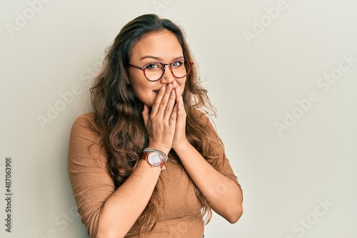 Young hispanic girl wearing casual clothes and glasses laughing and embarrassed giggle covering mouth with hands, gossip and scandal concept photo