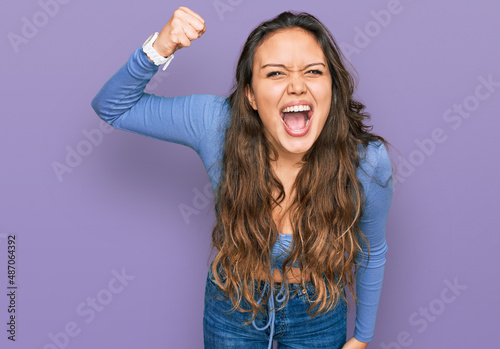 Young hispanic girl wearing casual clothes angry and mad raising fist frustrated and furious while shouting with anger. rage and aggressive concept.