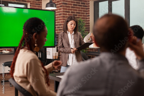 Businesswoman standing beside mock up green screen chroma key monitor with isolated display explaining partnership strategy working in startup office. Concept of businesspeople at work